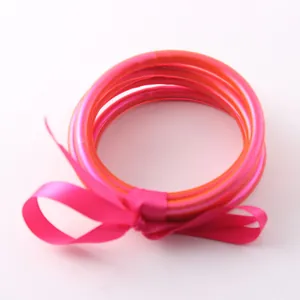 Dettaglio bracciali in tubo di silicone traslucido rosa e arancione con fiocco di seta