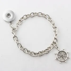 Detailansicht eines silbernen Kettenarmbands mit Druckknopfbasis und Steuerrad-Anhänger.