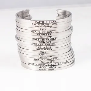 Macro view of a stack of stainless steel cuff bracelets with various engraved quotes.