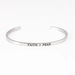 Detailed macro view of 'FAITH > FEAR' engraved on a minimalist silver stainless steel cuff.