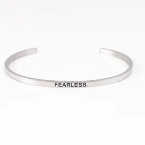 Close-up of minimalist stainless steel cuff bracelet with 'FEARLESS' engraving.