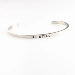 Detail shot of a minimalist silver stainless steel cuff bracelet with BE STILL engraving