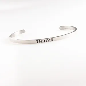 Macro view of silver stainless steel cuff bracelet with THRIVE engraved lettering