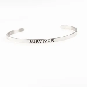 Detailed view of "SURVIVOR" engraving on silver stainless steel cuff bracelet.