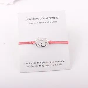 Detail van verzilverde puzzel hanger aan roze koord met autisme bewustzijn kaartje