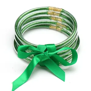 Close-up of five green glitter-filled silicone jelly bangles with a green satin bow