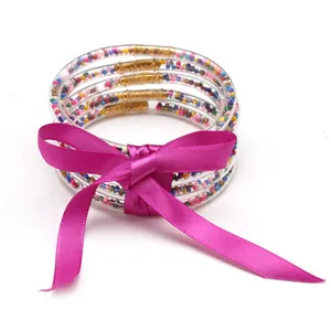 Primo piano di braccialetti jelly in silicone a 5 strati con perline e un fiocco magenta.
