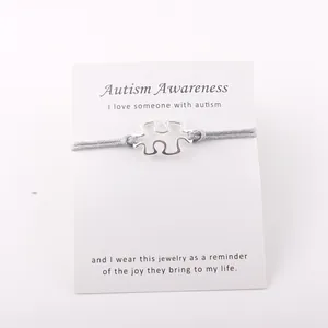 Detail van verzilverde Autism Awareness puzzel armband met grijs waskoord en een berichtkaart