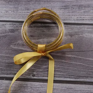 Detail of 7-layer gold glitter silicone jelly bangles set tied with a yellow silk ribbon.