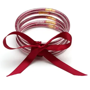 Close-up of pink glitter-filled silicone jelly bangles with a red silk ribbon bow