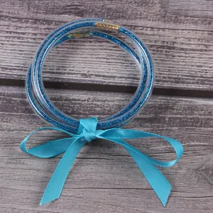 Vue détaillée de trois joncs en silicone bleu pailleté avec un ruban en satin.