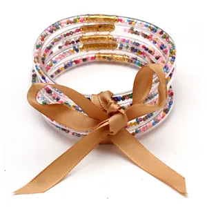 Dettaglio di braccialetti jelly a 5 strati con perline colorate e fiocco dorato