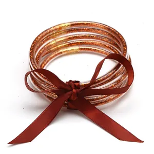 Close-up of five orange glitter silicone jelly bangles tied with a dark red satin bow