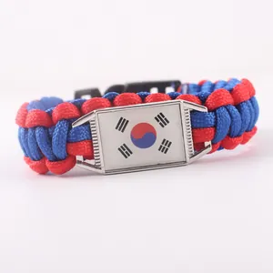 Dettaglio del charm bandiera sudcoreana su bracciale in paracord intrecciato rosso e blu.