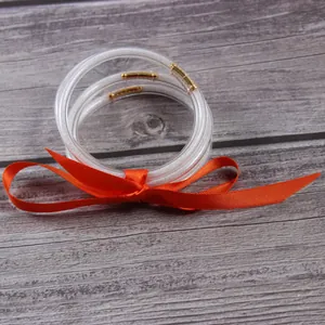 Detailed shot of clear glitter jelly bangles with orange ribbon on grey wood background.