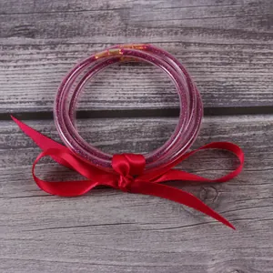 Détail de trois bracelets joncs en silicone à paillettes avec un ruban de satin rouge
