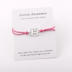 Detailopname van zilveren puzzelarmband met roze koord op Autism Awareness-kaart