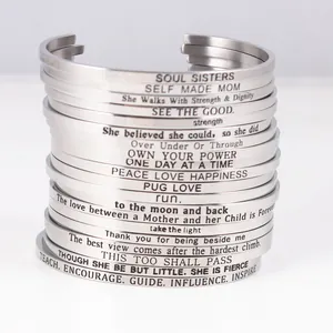 Close-up of stacked stainless steel cuff bracelets with motivational engravings.