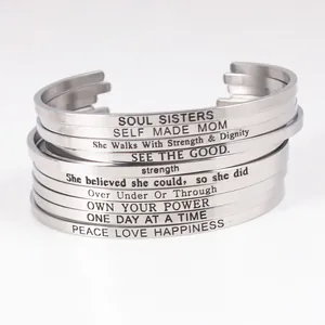 Close-up of stacked silver stainless steel cuff bracelets with inspirational engravings