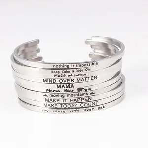 Close-up of stacked stainless steel cuff bracelets with various engraved mantra quotes