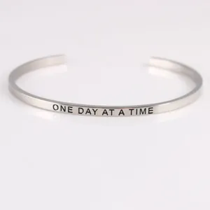 Close-up detail of silver stainless steel bracelet engraved with One Day At A Time