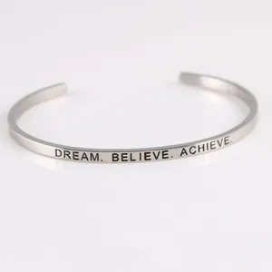 Macro view of 'DREAM. BELIEVE. ACHIEVE.' engraving on a minimalist stainless steel cuff bracelet