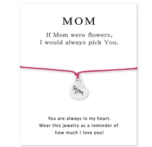 Detailed view of a pink braided bracelet with a heart 'Mom' charm on a gift message card.