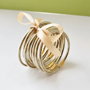 Detailed view of nine gold glitter jelly bangles tied with a decorative cream ribbon bow