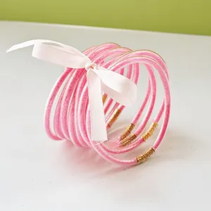Close-up of 9-piece pink glitter jelly bangles tied with a decorative white ribbon bow