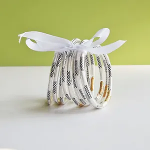Close-up of nine jelly bangles with black patterns and gold accents tied in white ribbon