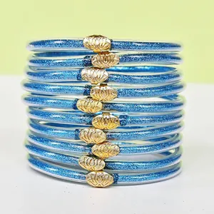 Dettaglio di 10 braccialetti jelly blu glitterati con chiusure a forma di loto dorato.