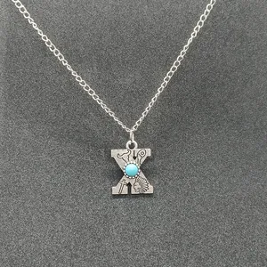 Close-up detail of a vintage silver chain necklace featuring a turquoise initial X pendant