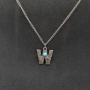 Macro view of a vintage silver necklace with a W-shaped pendant and turquoise stone.
