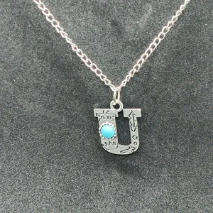 Close-up of vintage silver 'U' initial pendant with turquoise and stamped patterns.