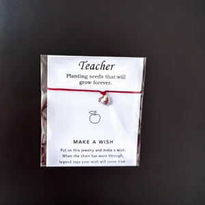 Nahaufnahme des roten Armbands mit Apfel-Anhänger auf einer Wunschkarte für Lehrer