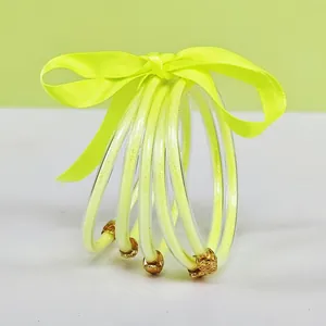 Close-up of five-layer fluorescent yellow glitter jelly bangles with golden lotus charms