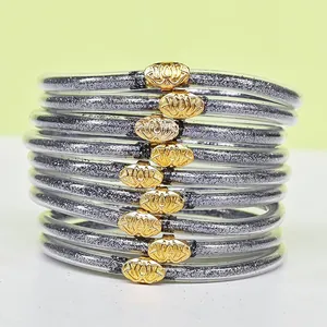 Gros plan de 9 bracelets superposables en silicone pailleté argenté avec boucles lotus dorées.