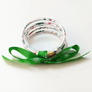 Detalle de pulseras navideñas de silicona multicapa con un lazo de cinta verde de copos.