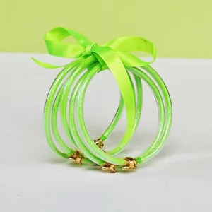Macro view of five green glitter-filled silicone tube bangles tied with a ribbon