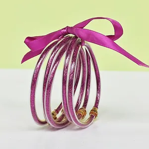 Close-up of five purple glitter silicone bangles tied with a matching silk ribbon bow