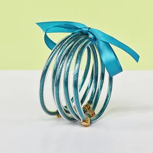 Detailed view of five-piece teal glitter silicone bangles tied with a blue satin ribbon
