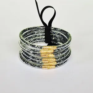 Close-up of 6-layer glitter-filled PVC bangles with gold accents and black ribbon.