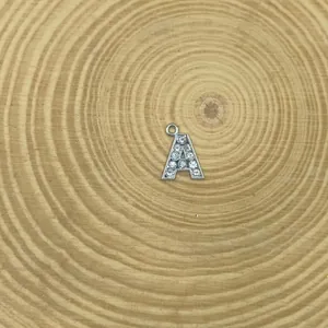 Detailed macro view of silver-tone rhinestone letter A pendant on a natural wood surface
