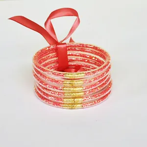Detail view of 6-layer glitter silicone bracelets with red satin ribbon bow and gold links.