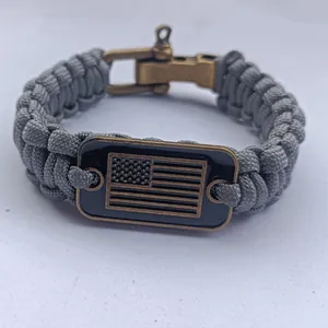 Detalle de una pulsera de paracord gris con una placa de bronce de la bandera de EE. UU.