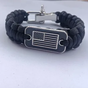 Detalle de pulsera de paracord negro con placa de bandera de EE. UU. y cierre en U plateado.