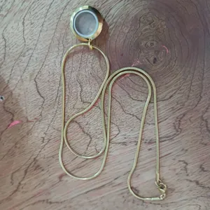 Vue détaillée d'un collier médaillon flottant en acier doré sur une surface en bois naturel