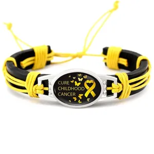 Detalle de la pulsera de concienciación sobre el cáncer infantil con cinta amarilla y cuero.