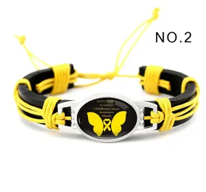 Detalle de pulsera de cuero negro tejida a mano con cordón amarillo y motivo de cánc