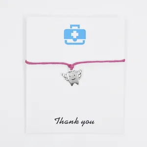 Detail of a pink wax cord bracelet featuring a silver winged tooth charm on a card.